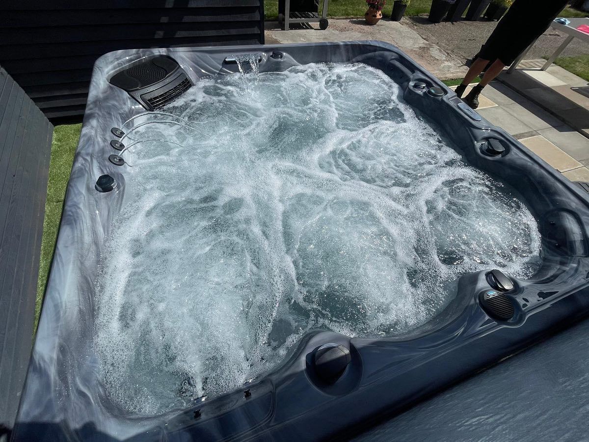 Hot tub with bubbling water, dark gray exterior, outdoors on patio.