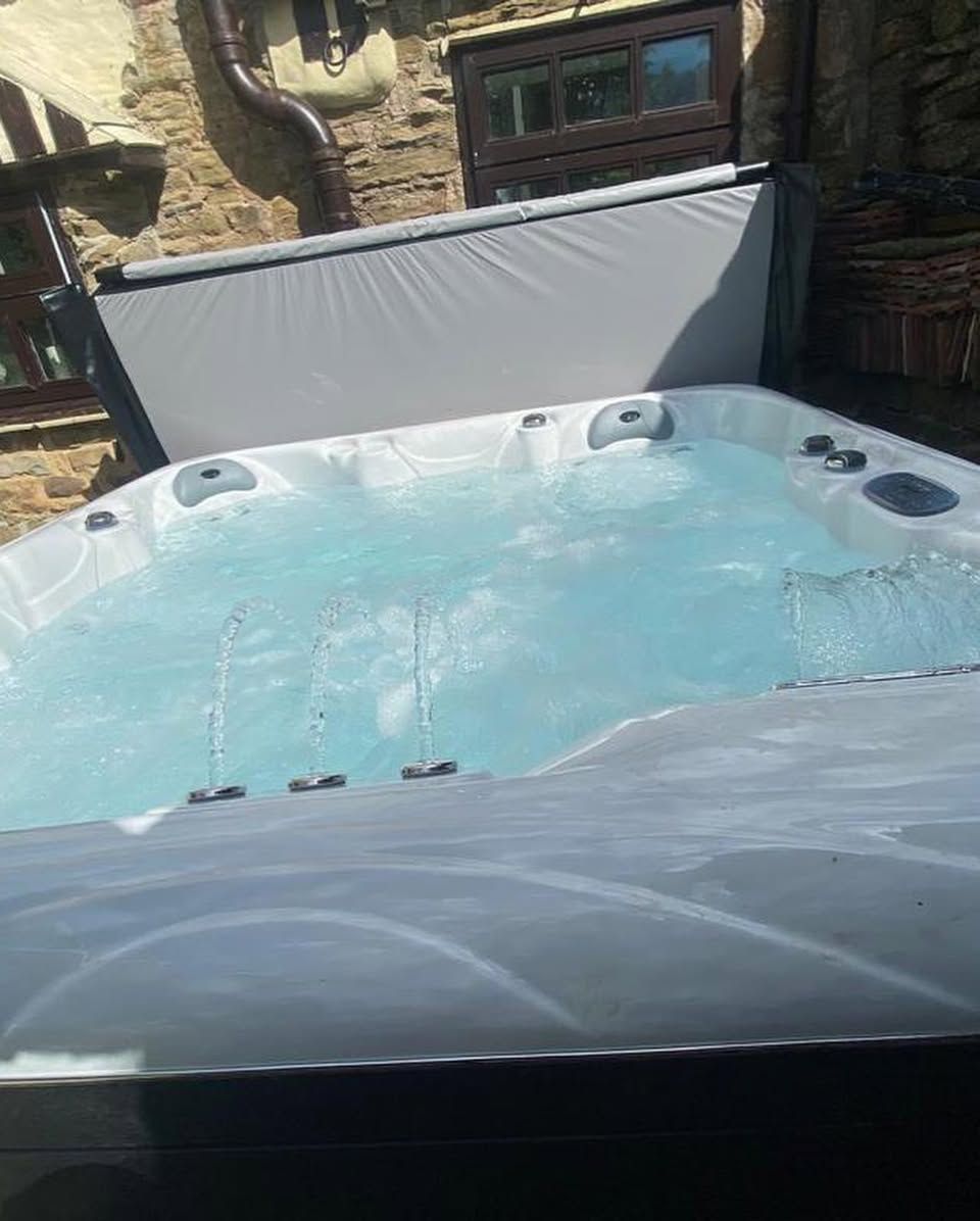 Hot tub filled with water, cover partially open. Stone building in the background.