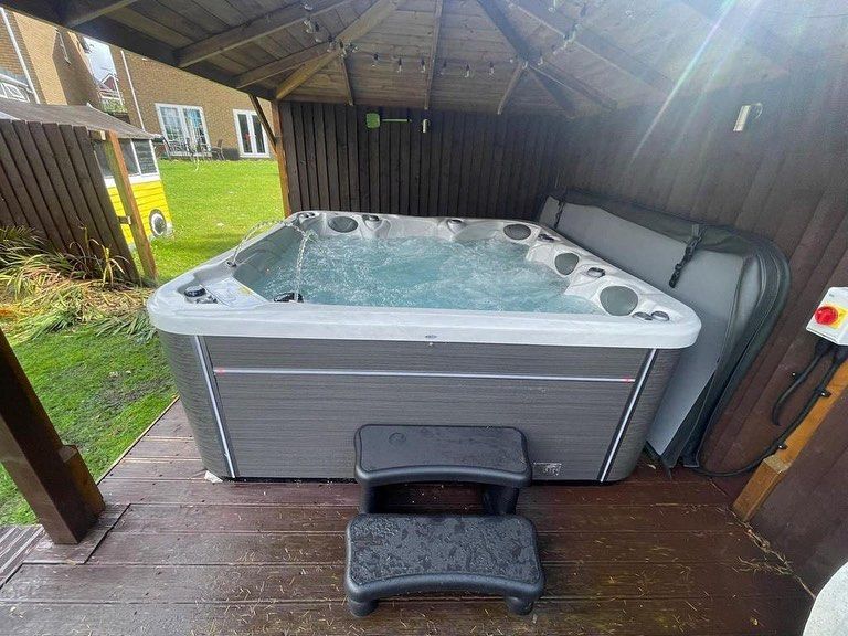 Hot tub in a wooden gazebo, water bubbling. Black steps in front.