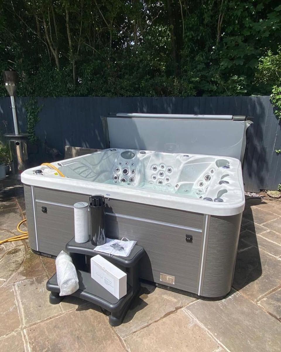 A gray hot tub sits on a brick patio. The cover is open. A small step stool with cleaning supplies is in front.