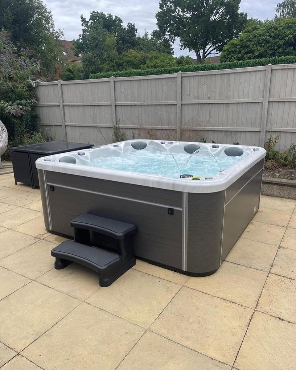 Hot tub with bubbling water on a patio with steps. A dark grey exterior and a light-colored fence are in the background.