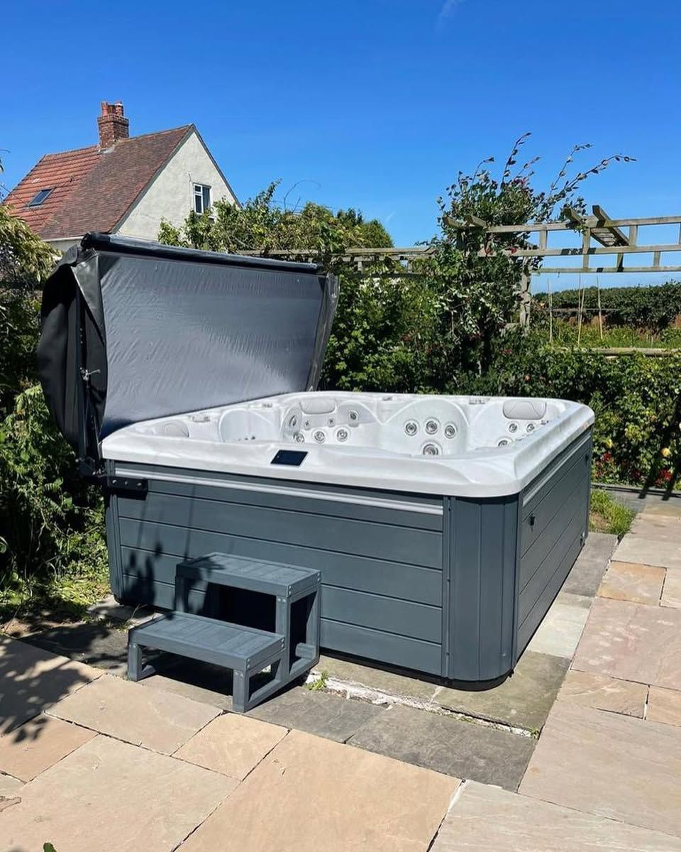 A gray hot tub with an open cover, gray steps, and a sunny outdoor setting.