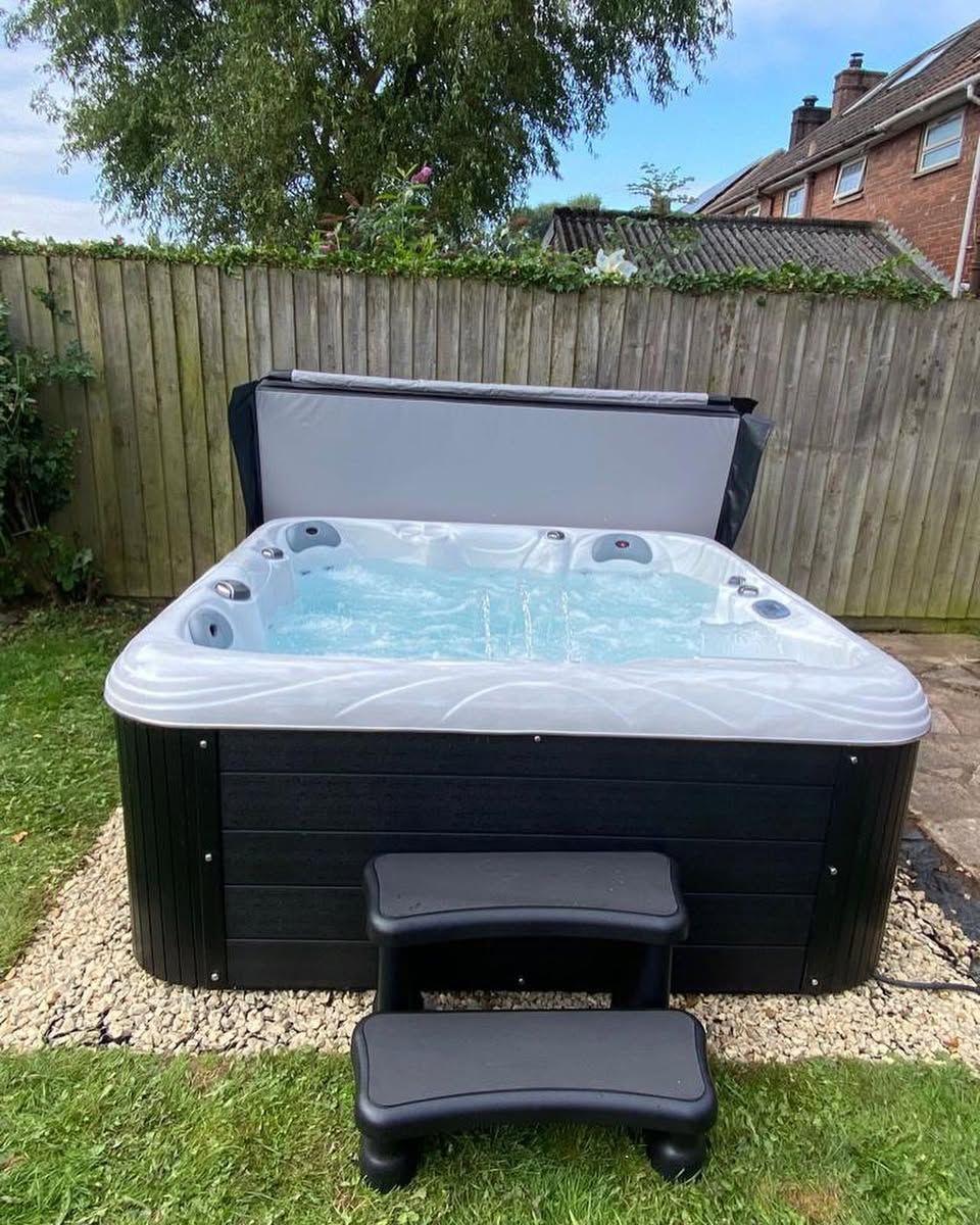 Hot tub with bubbling water, steps, and cover in a backyard with wooden fence.