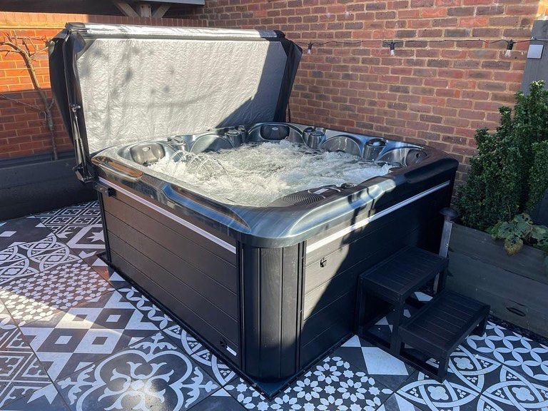 Hot tub with bubbling water, cover open, on patterned patio. Brick wall in the background.