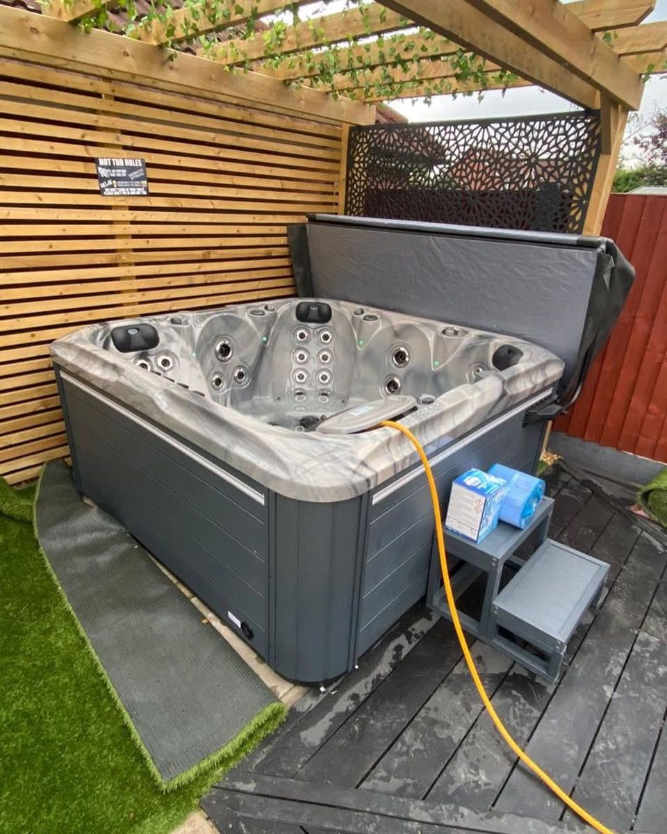 Hot tub on a wooden deck next to a wood fence, with steps and a partially open cover.