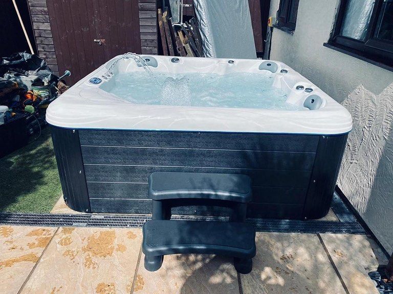 Hot tub with dark gray exterior, filled with water, next to a step.
