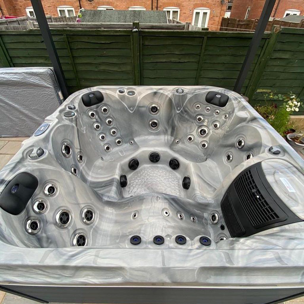 Grey and white marbled hot tub with black jets and controls, outdoors.