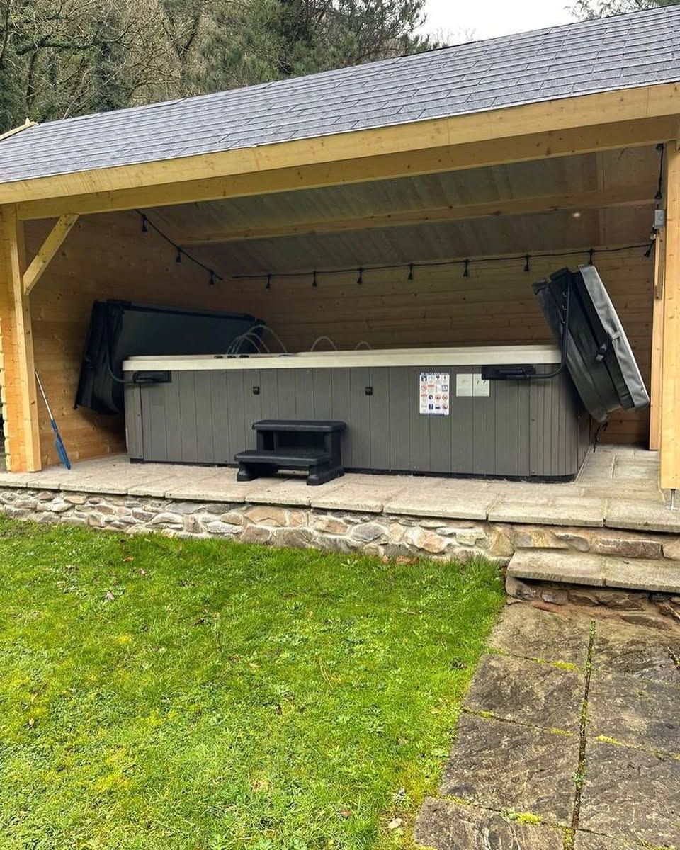 Hot tub under a wooden shelter, with steps and partially open covers.  Green lawn, stone patio.