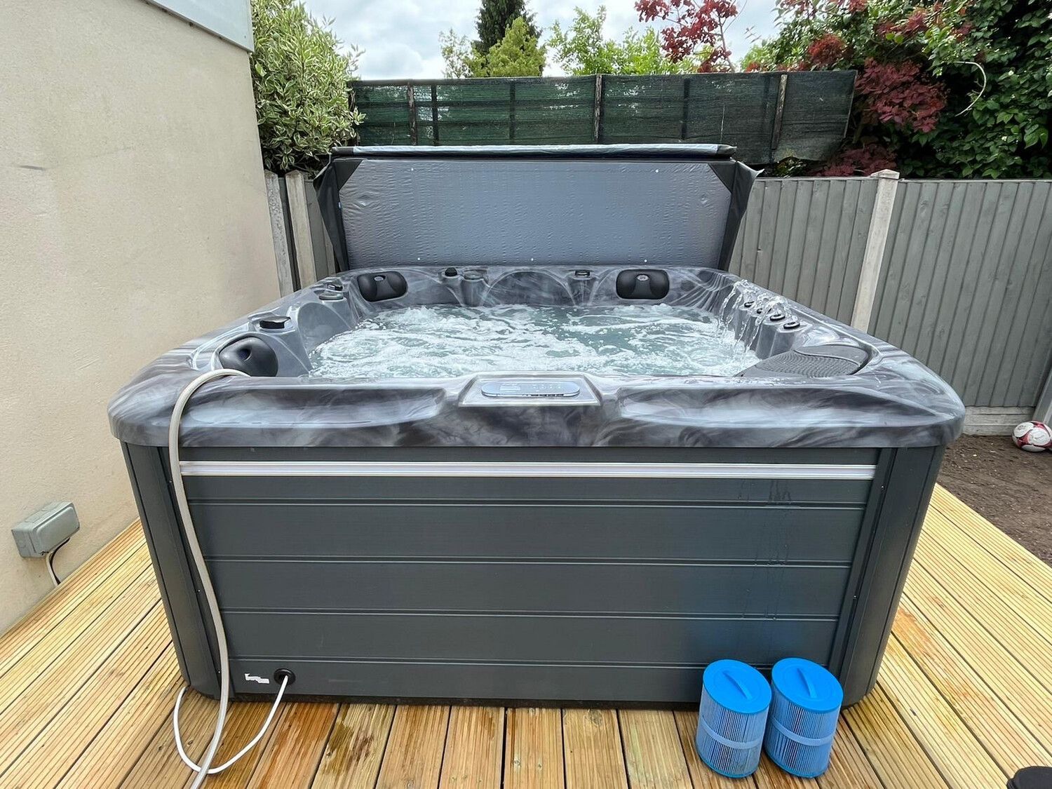 A dark gray hot tub with jets bubbling, lid open, on a wooden deck outdoors.