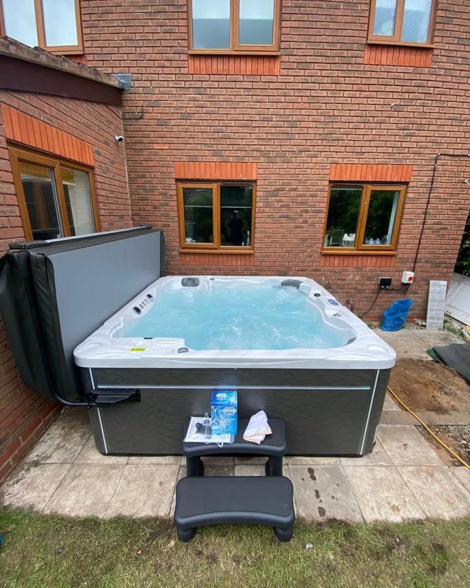 Hot tub on patio, next to a brick building. The cover is open.