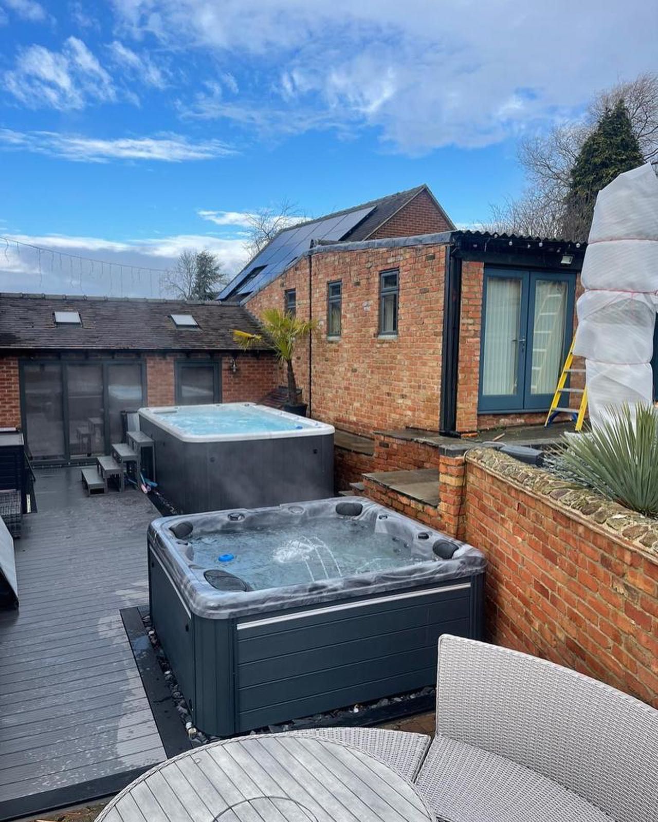 Two hot tubs on a patio with brick buildings in the background. Cloudy sky overhead.