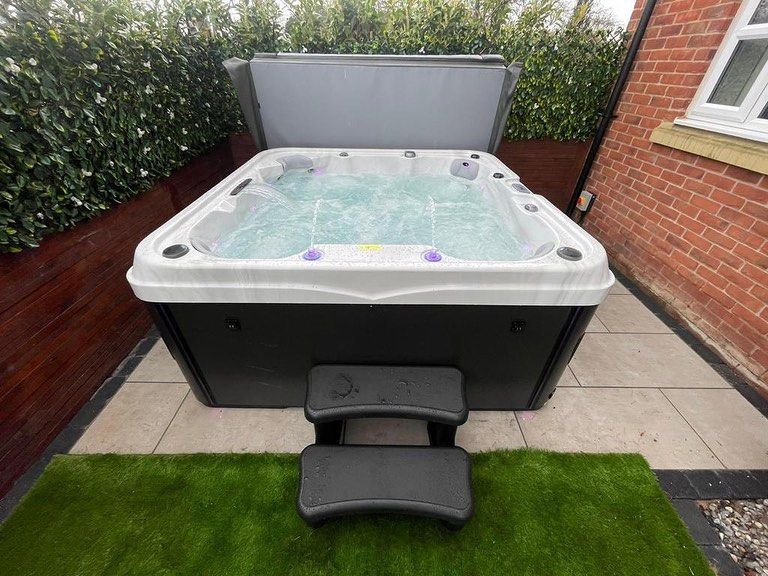 Hot tub with open cover, steps in front, set on patio with green turf.