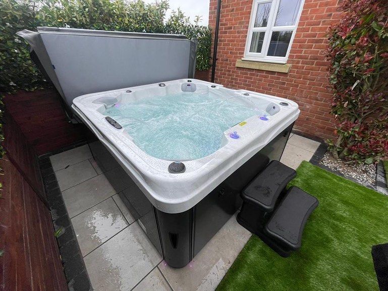 Hot tub with open cover, bubbling water, surrounded by brick, steps, and greenery.