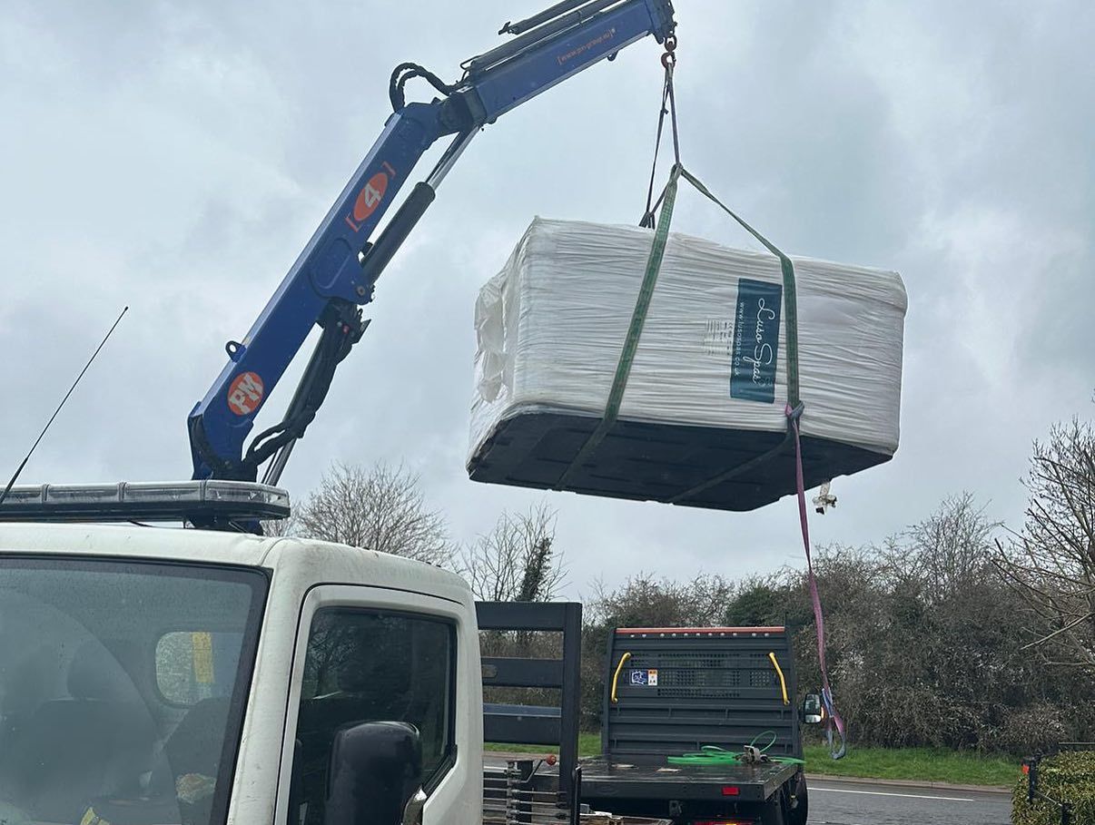A wrapped hot tub is lifted by a truck crane, preparing to be delivered.