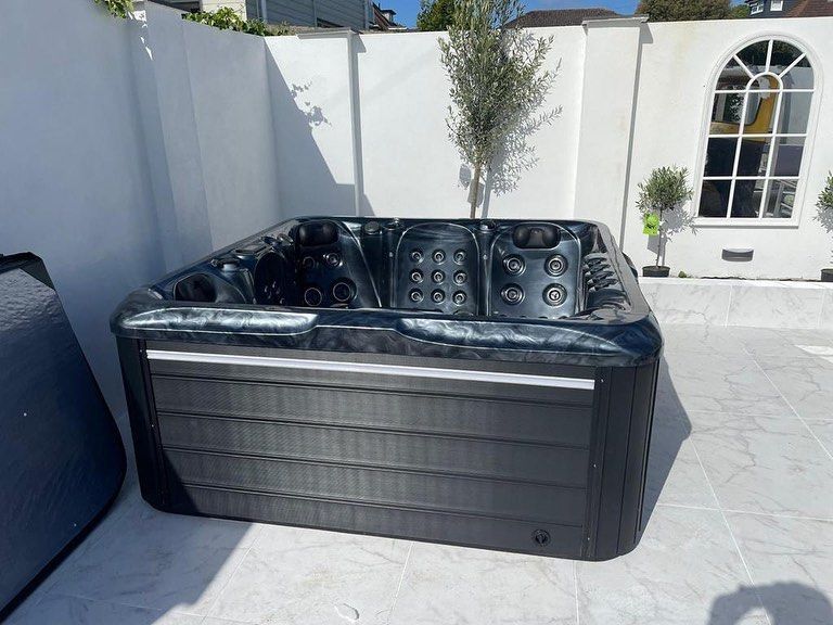 A black hot tub on a patio, against a white wall with an arched window.