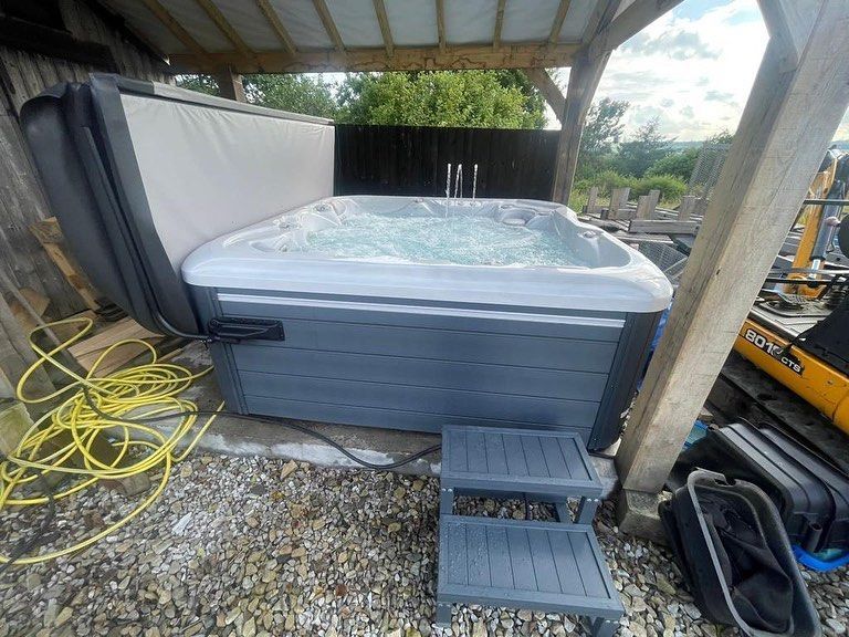 Hot tub with bubbles, grey frame, under a wooden roof, steps in front.