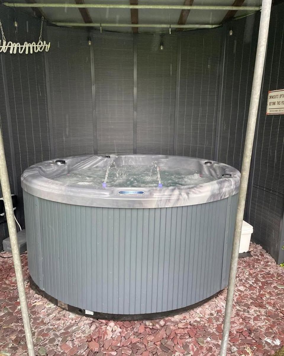 Gray hot tub in a screened enclosure, on a bed of red gravel.