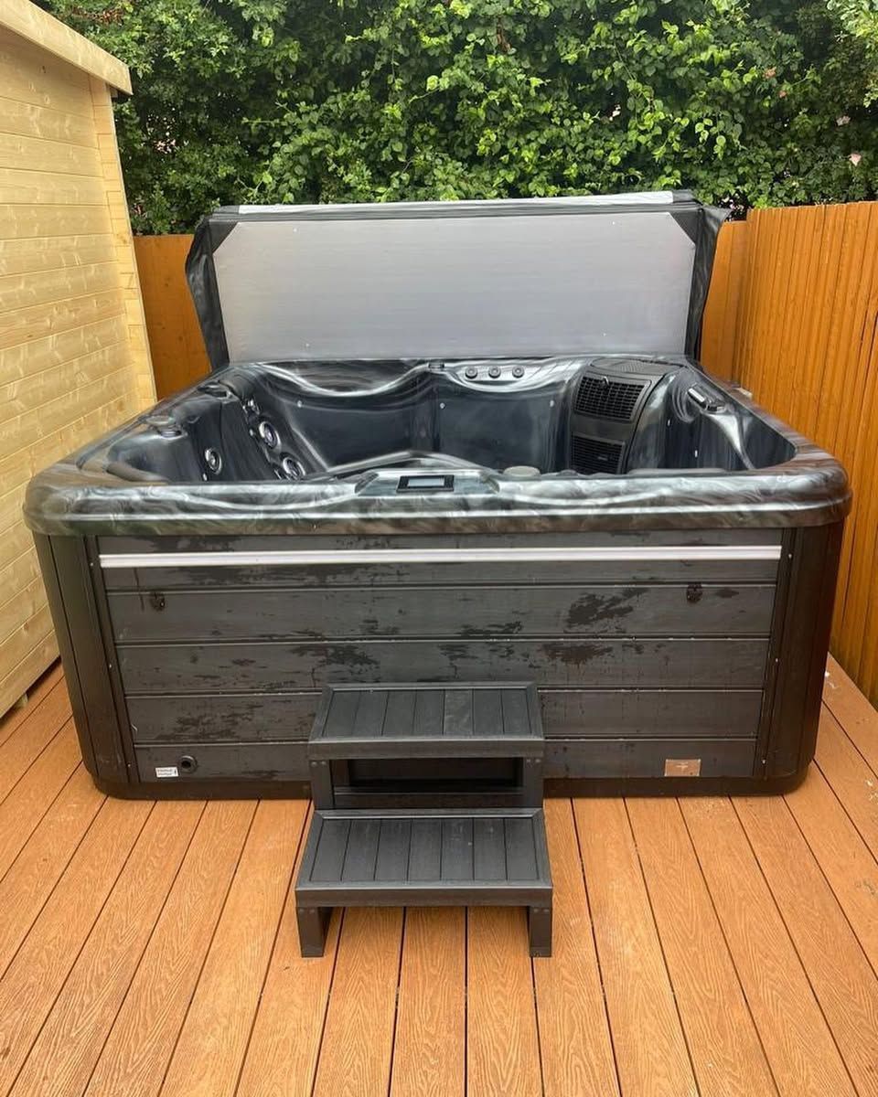 Dark hot tub with gray cover open, on wooden deck with steps.