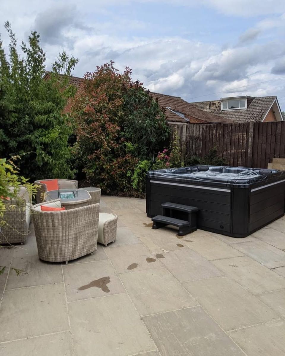 Patio with a hot tub, outdoor furniture, and lush greenery under a cloudy sky.