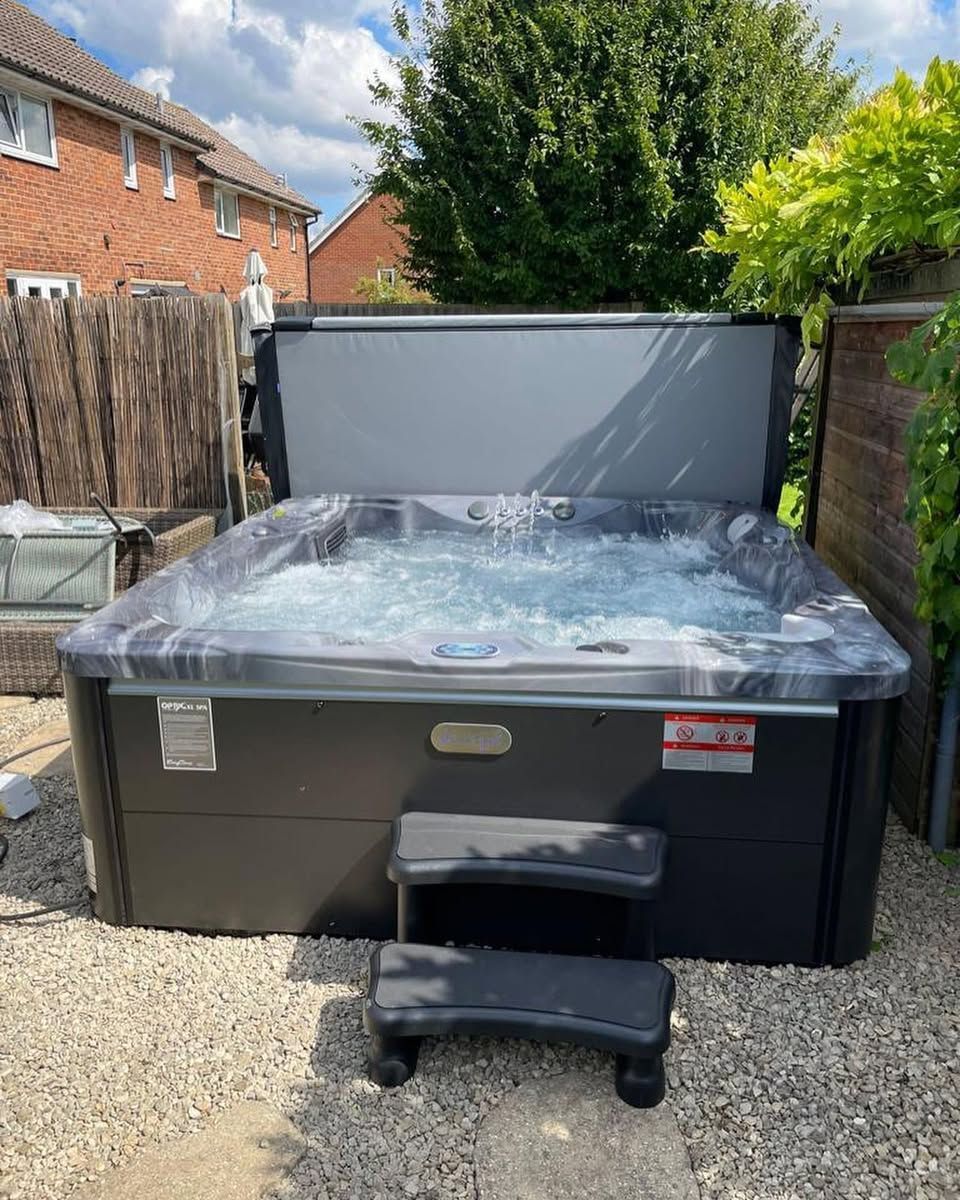 Hot tub with open cover, bubbling water, and small step in a backyard.