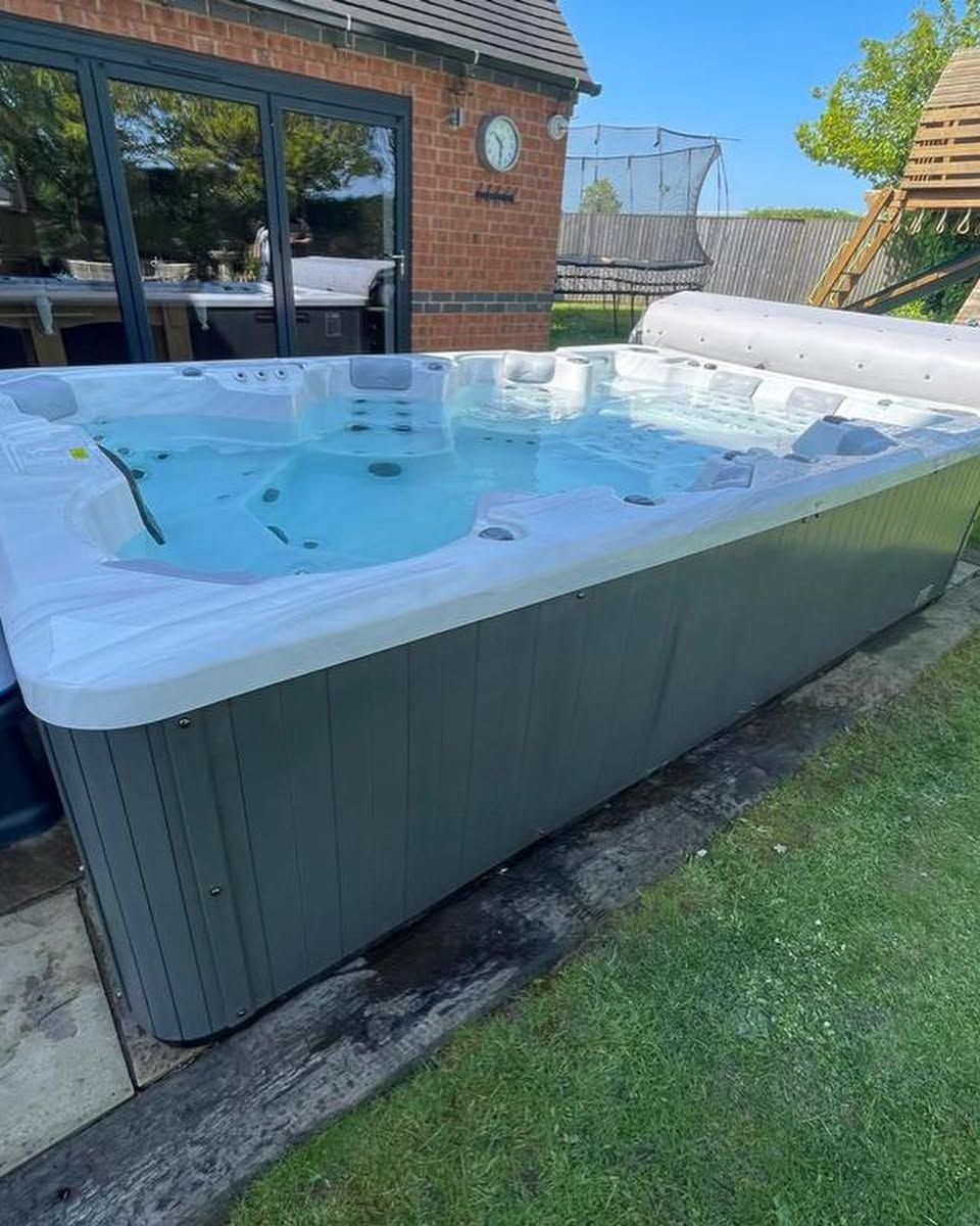 A rectangular hot tub with bubbling water, set outside on a lawn. Gray exterior, white rim, and partially covered.