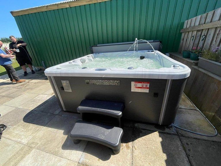 Hot tub with steps on a patio, two people in the background.