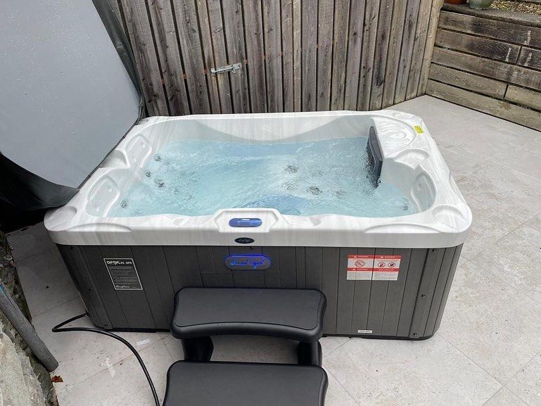 Hot tub with bubbly water, steps in front. Gray siding and wooden fence in the background.