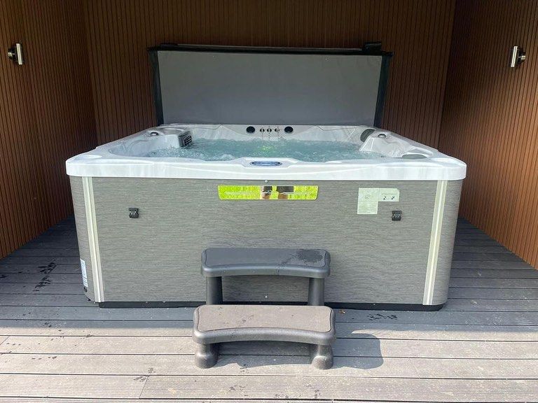 Hot tub with open cover, two-step stool in front, enclosed in wooden structure.