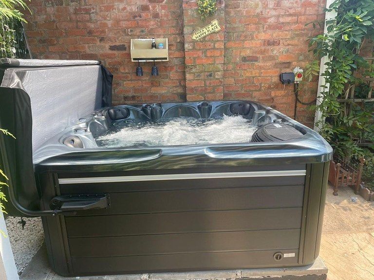 Black hot tub with bubbling water next to a brick wall, cover partially open.