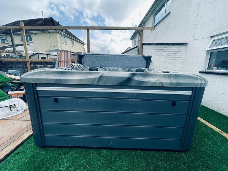Gray hot tub on green turf, next to a white building.