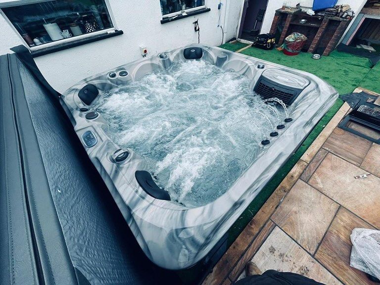 A bubbling hot tub on a patio with a cover partially open.