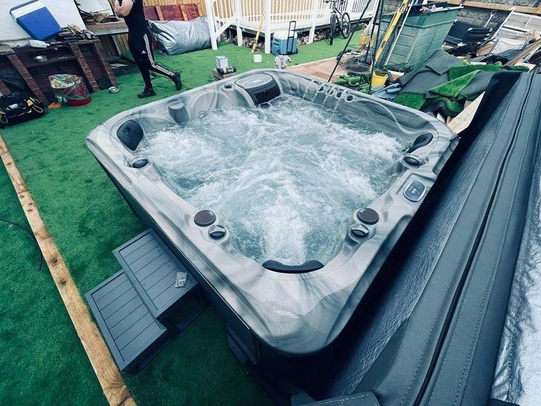 Hot tub filled with water, bubbling. Outside on artificial grass with steps.