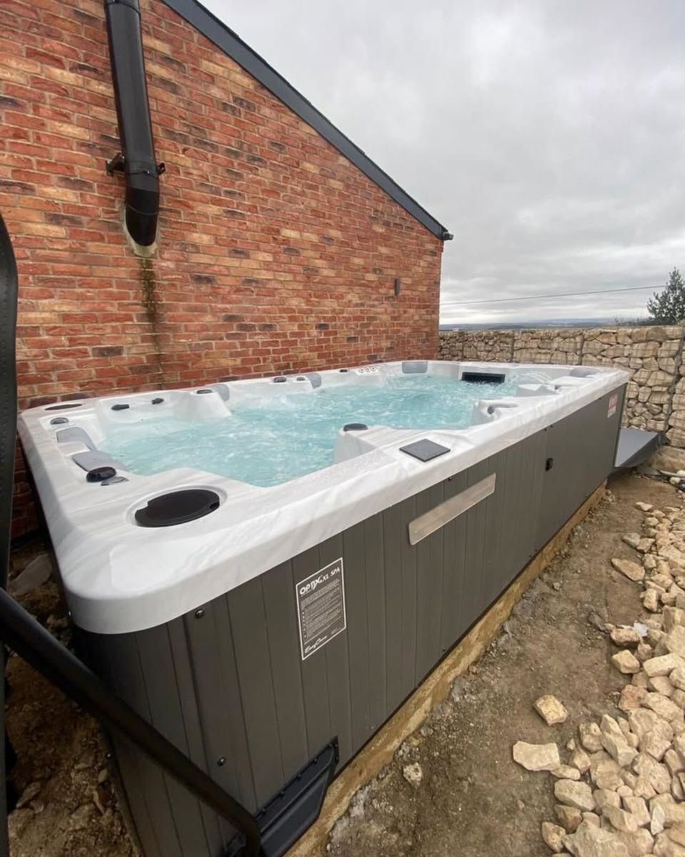 Outdoor hot tub next to a brick building. Gray siding, white trim, and a cloudy sky.