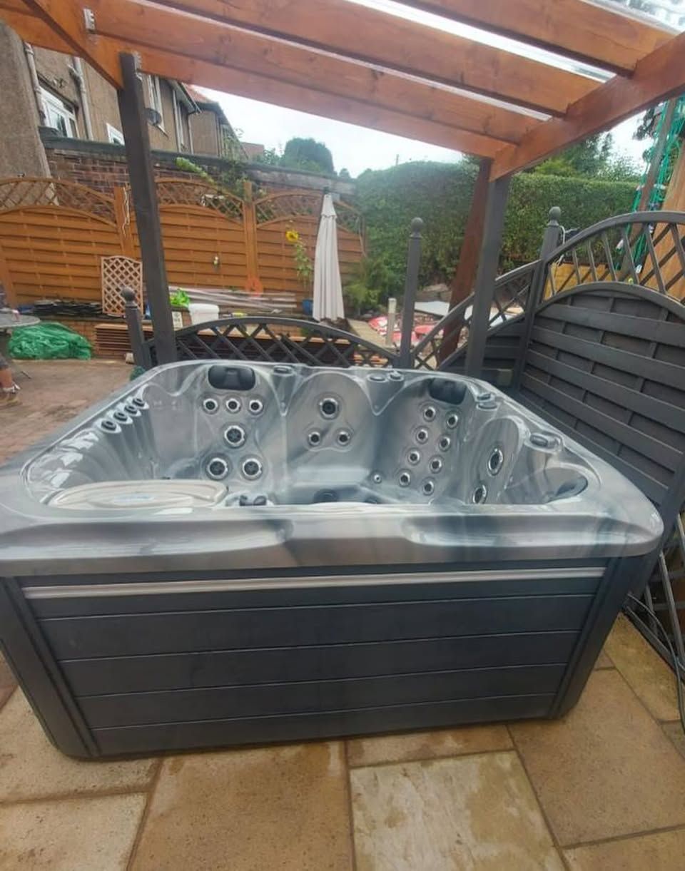 Hot tub under a wooden pergola, on a patio. Gray and dark wood tones, outdoor setting.
