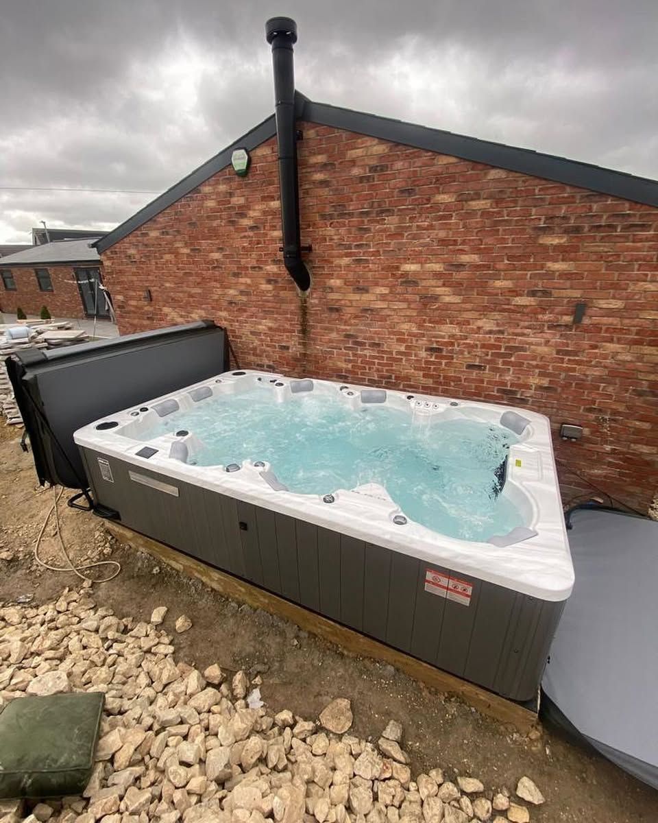 Hot tub with clear water, next to a red brick wall, and an open cover on the side.