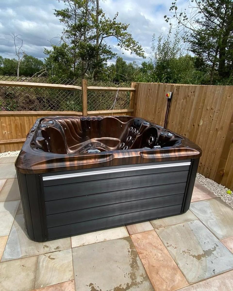 Hot tub on a stone patio with a wood fence and trees in the background.