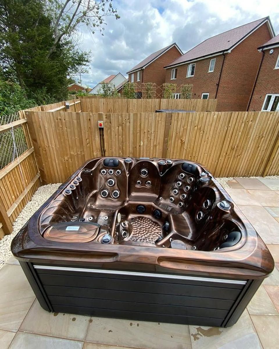 Bronze hot tub on a stone patio, with a wooden fence and houses in the background.