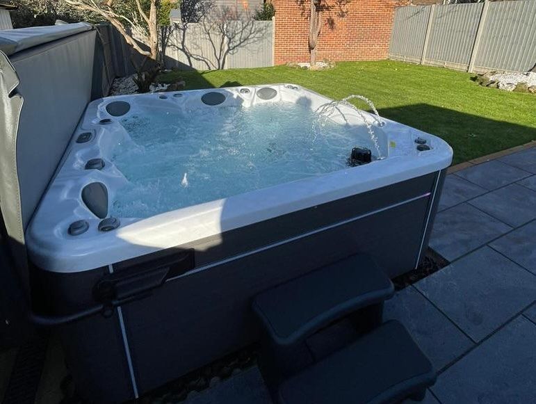 A triangular hot tub on a patio with bubbling water, steps, and a grassy backyard.
