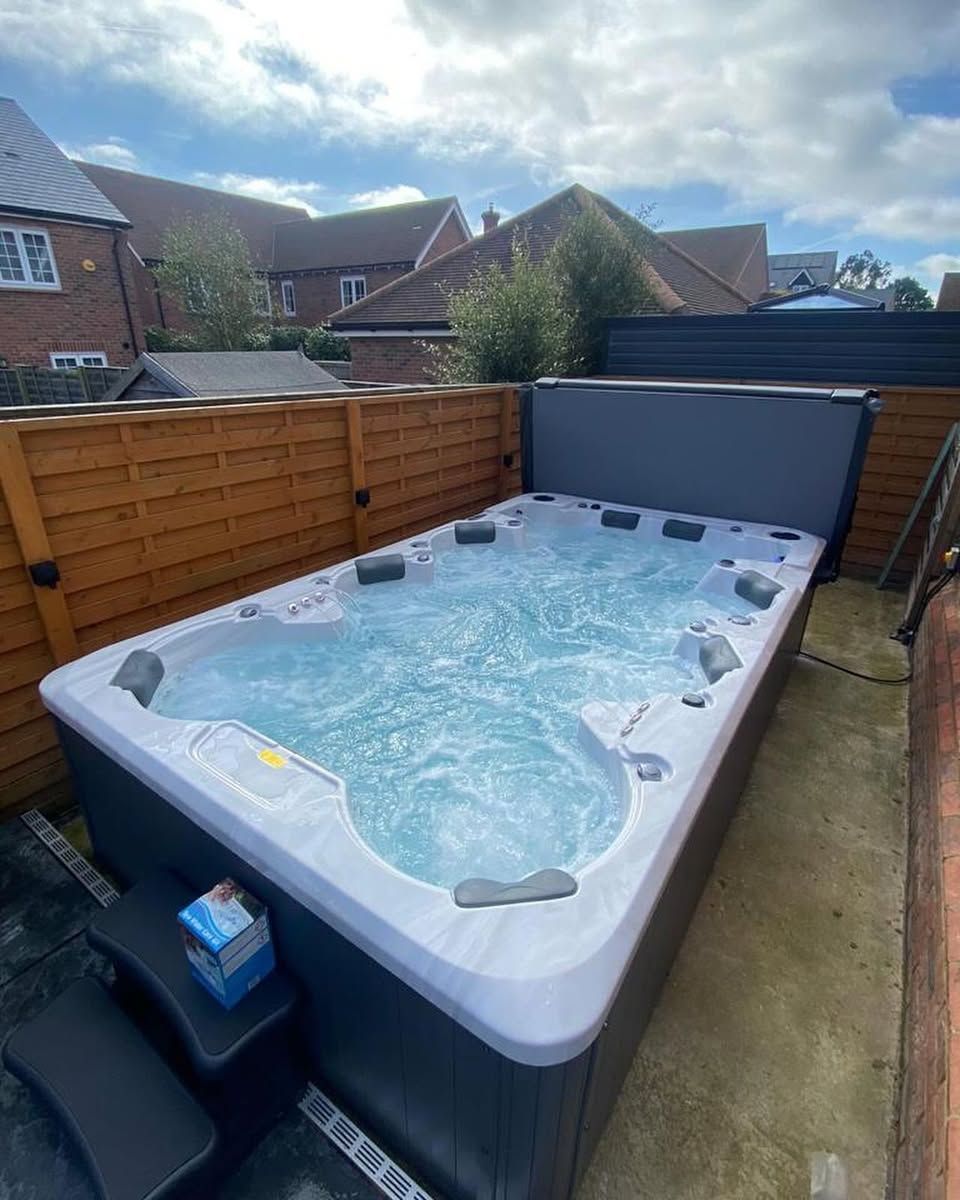 A rectangular swim spa filled with water, surrounded by a wooden fence, in a backyard setting.