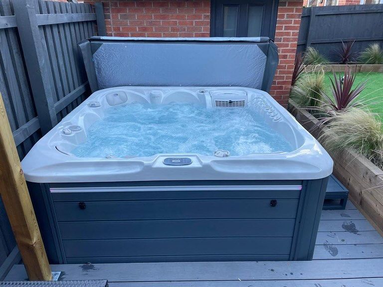 A bubbling gray hot tub, cover partially open, in a backyard setting.