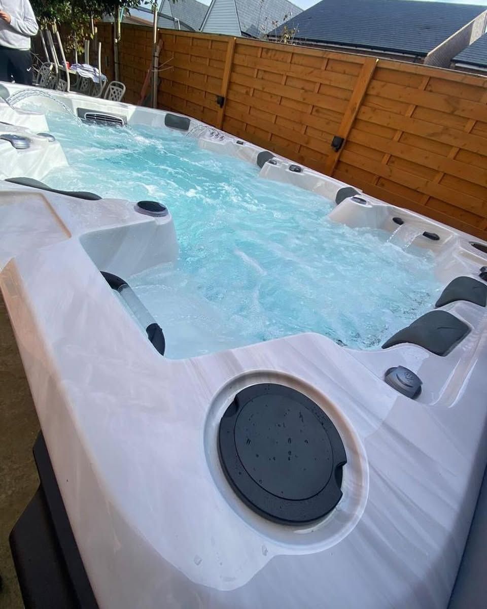 A rectangular hot tub with bubbling water and a wooden fence backdrop.