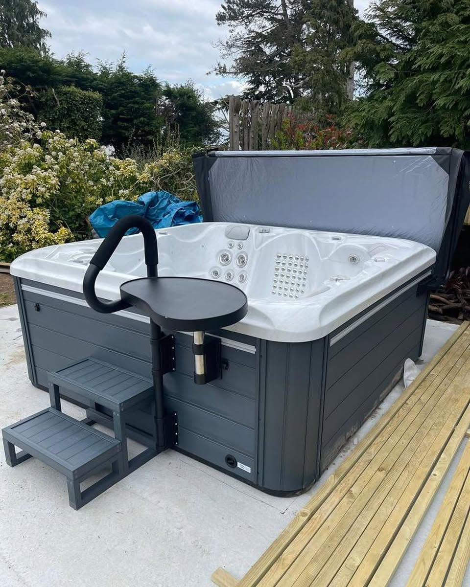 Hot tub with gray steps and a side table, outdoors. The cover is open.