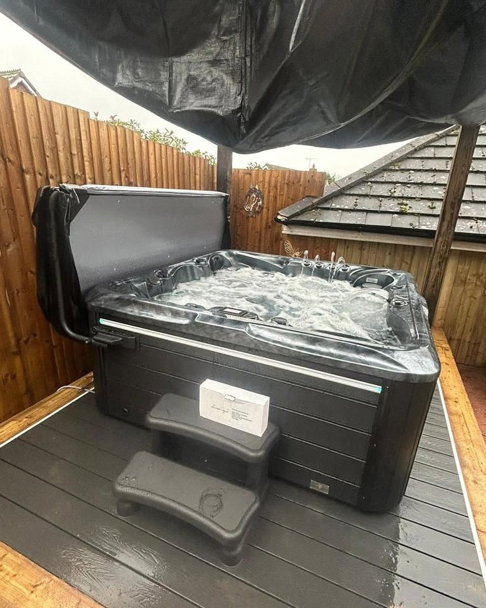 Hot tub on wooden deck, covered by a black canopy. Bubbling water and steps are visible.