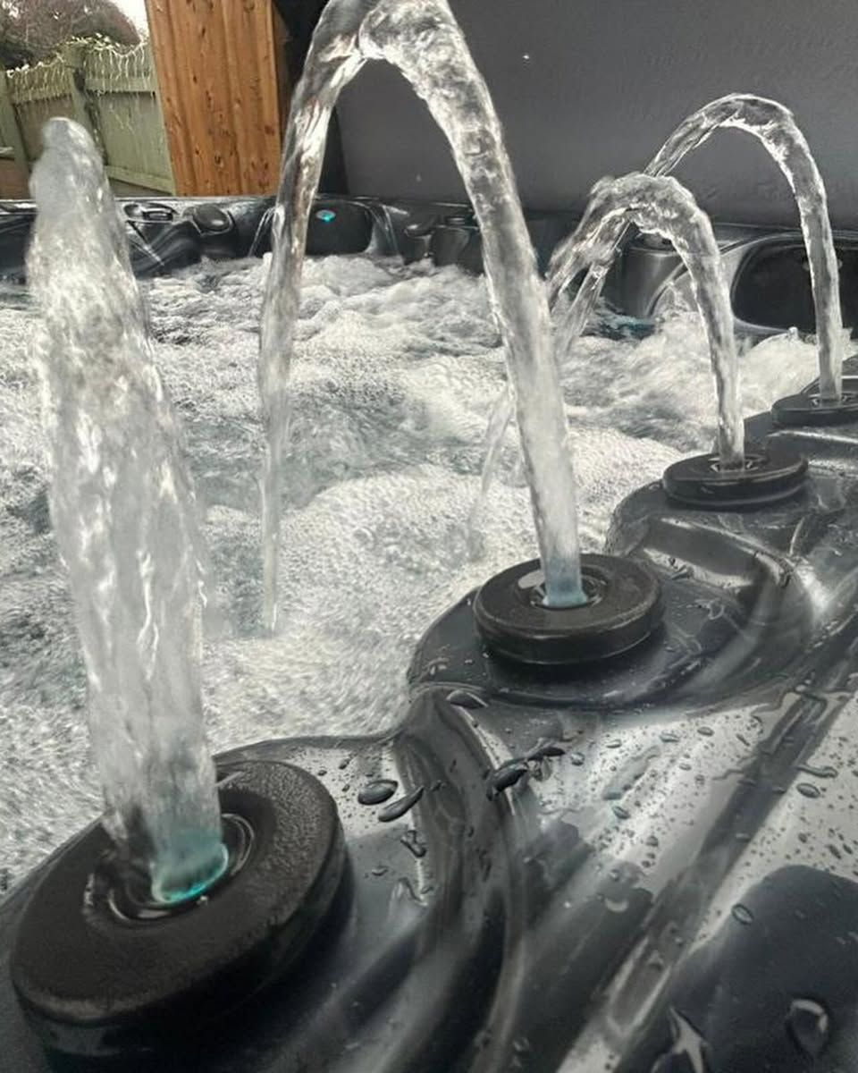 Water jets arching over a foamy spa interior, black trim, wooden post in background.