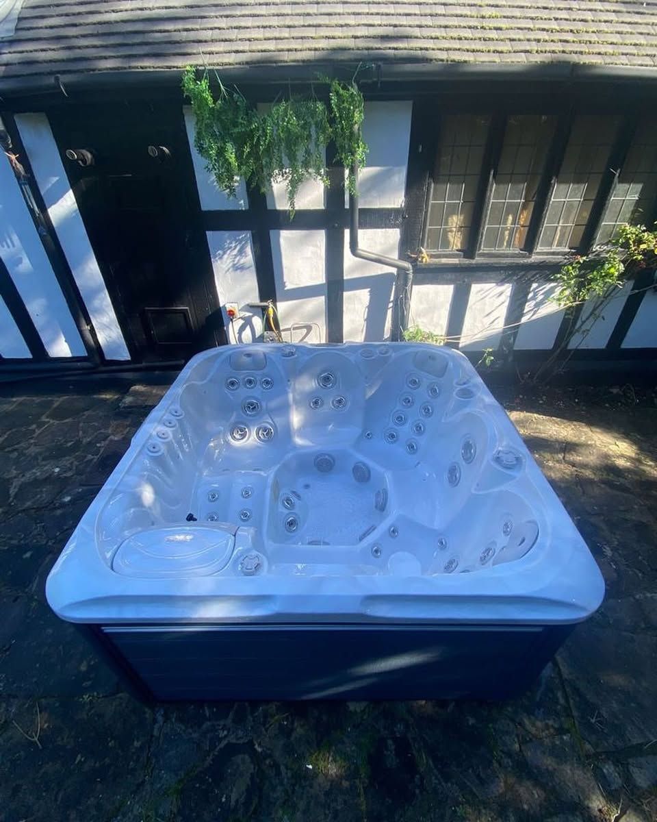 Square hot tub with white interior, black exterior, in front of a house with white and black Tudor-style exterior.