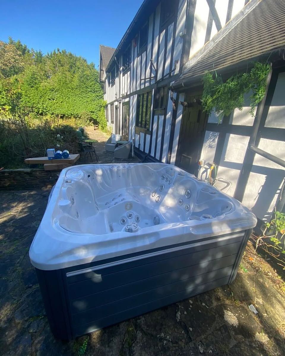Hot tub outside a black and white Tudor-style house on a sunny day.