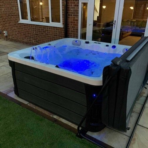 Hot tub with blue lights, bubbling water on a patio beside a house. Cover open.