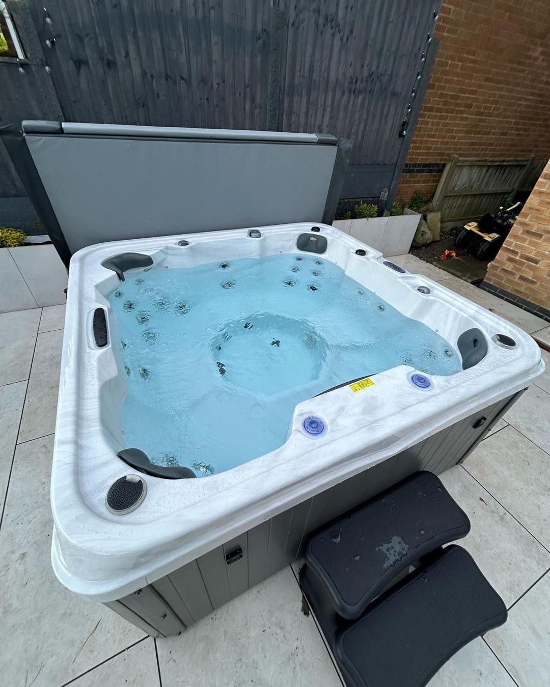 Hot tub filled with water, open cover, on a patio, with steps.