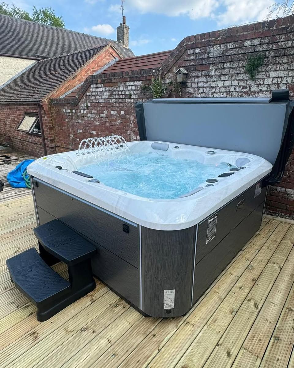 Hot tub with open cover, bubbling water, on a wooden deck, next to steps and a brick wall.
