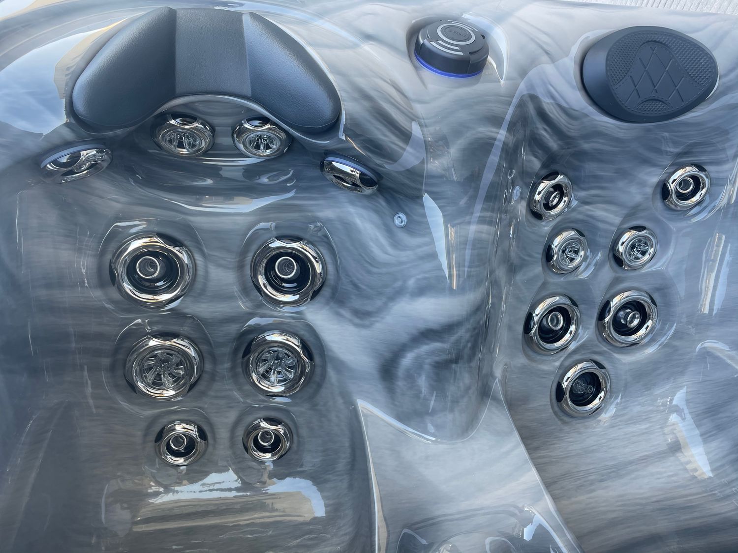 Close-up of a hot tub interior with gray marbled shell, water jets, and control panel.